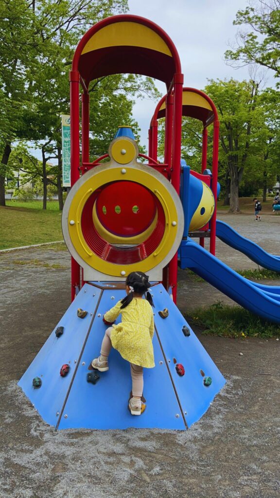 岩槻城址公園のわんぱく広場内にある汽車のデザインの幼児向け複合遊具のボルダリング遊具で遊ぶ子供