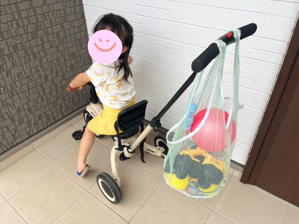 ヤトミののりかえ三輪車の押し棒におもちゃ入れの袋がかかっています